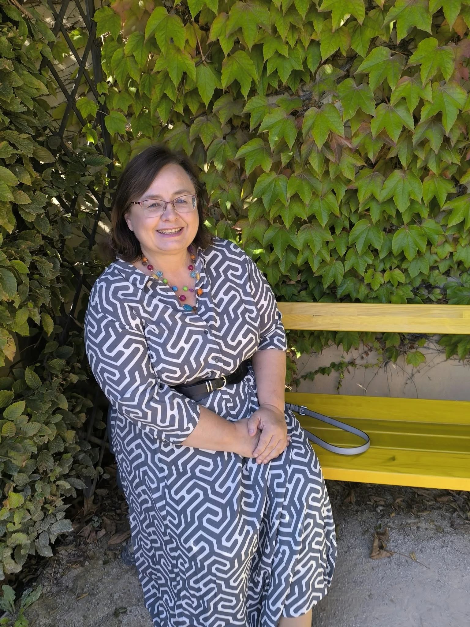 Jitka Štádlerová sedí na žluté lavičce před zelenými listy.
